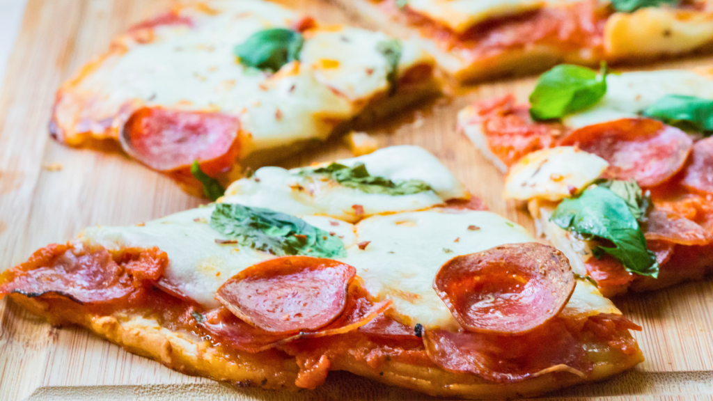Easy pepperoni and salami pizza with melted mozzarella and fresh basil, sliced on a wooden cutting board.