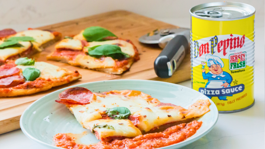 Pepperoni and salami pizza slice on a plate with Don Pepino Pizza Sauce for dipping and the sliced pizza in the background.