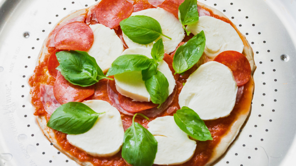 Unbaked pizza topped with Don Pepino Pizza Sauce, pepperoni, Italian salami, fresh mozzarella, and basil.